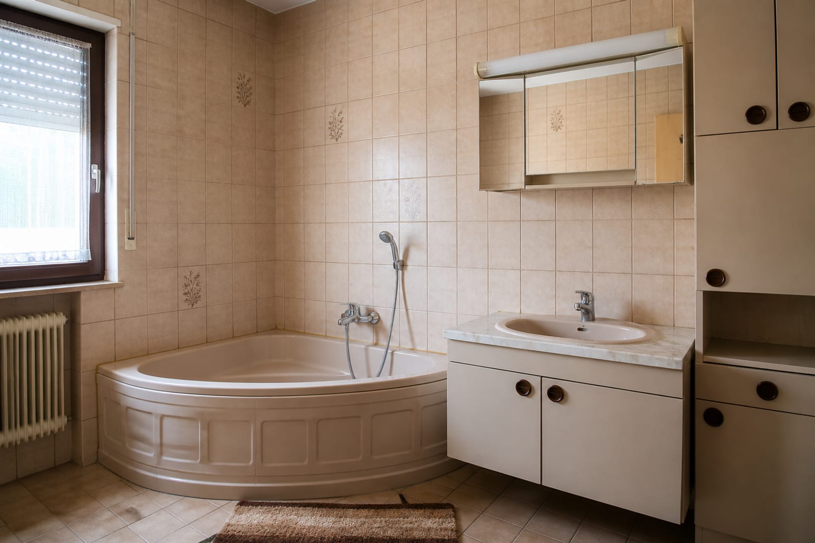 Dasselbe Bad vor der Sanierung mit beigen Fliesen und Eckbadewanne